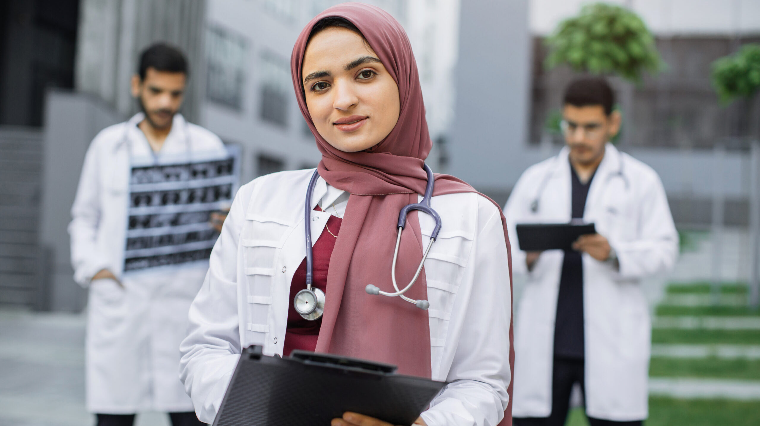 Confident young doctor wearing stethoscope standing before medical team outdoors.
